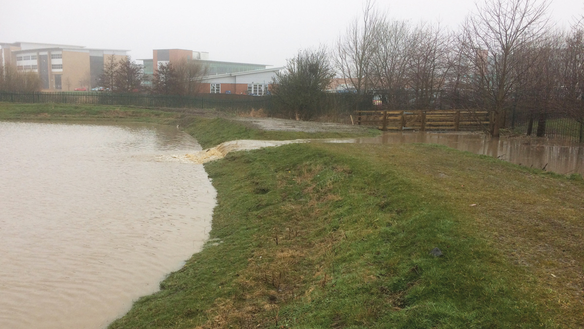 The attenuation basin at Longbenton Community College in operation during March 2018. The levels in Forest Hall Letch re-raised and the basin is filling as the flows from the letch spill over the weir - Courtesy of Esh Stantec